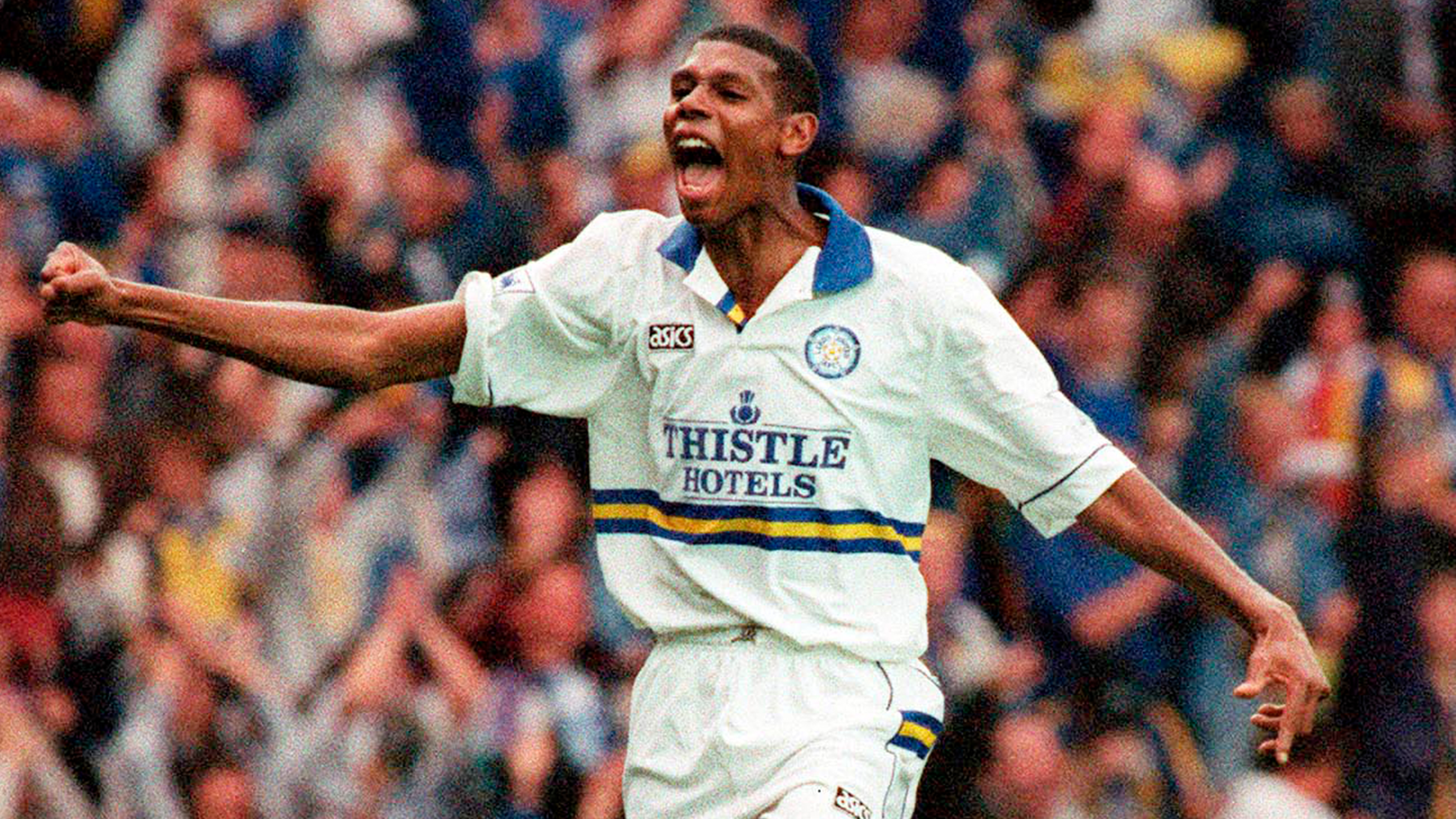 Leeds player Carlton Palmer celebrating on field in front of a backdrop of supporters. He is wearing the leeds home kit of 1994. 